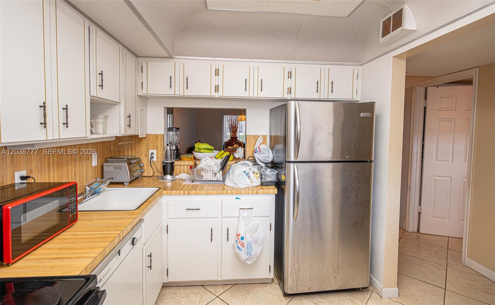 A kitchen features white cabinets, a stainless steel refrigerator, and wood-patterned laminate countertops — 3531 Inverrary Dr # 108, Lauderhill FL 33319, LAUDERHILL, FL