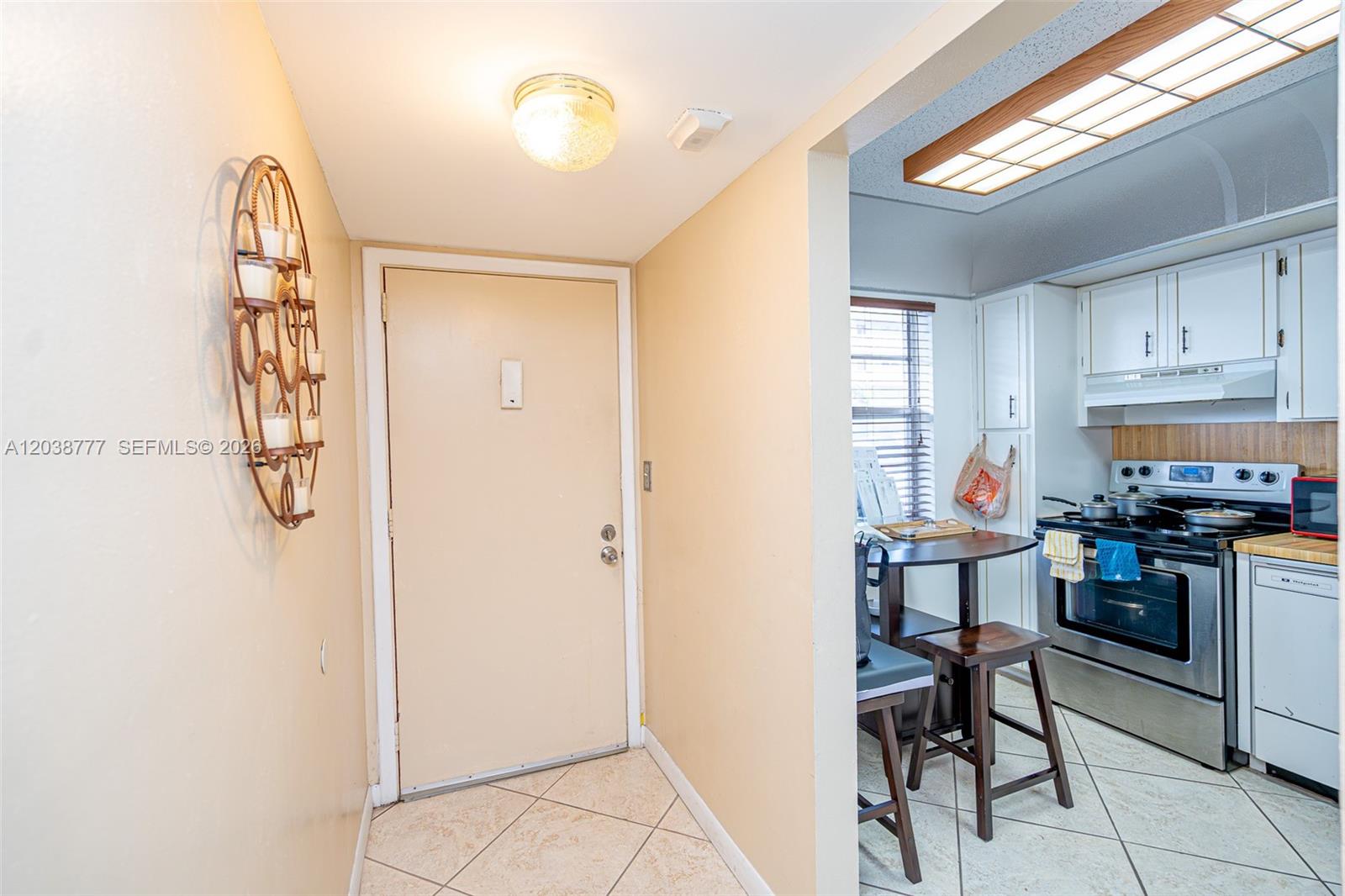 An entryway with a wall-mounted candle holder leads into a kitchen with white cabinets — 3531 Inverrary Dr # 108, Lauderhill FL 33319, LAUDERHILL, FL