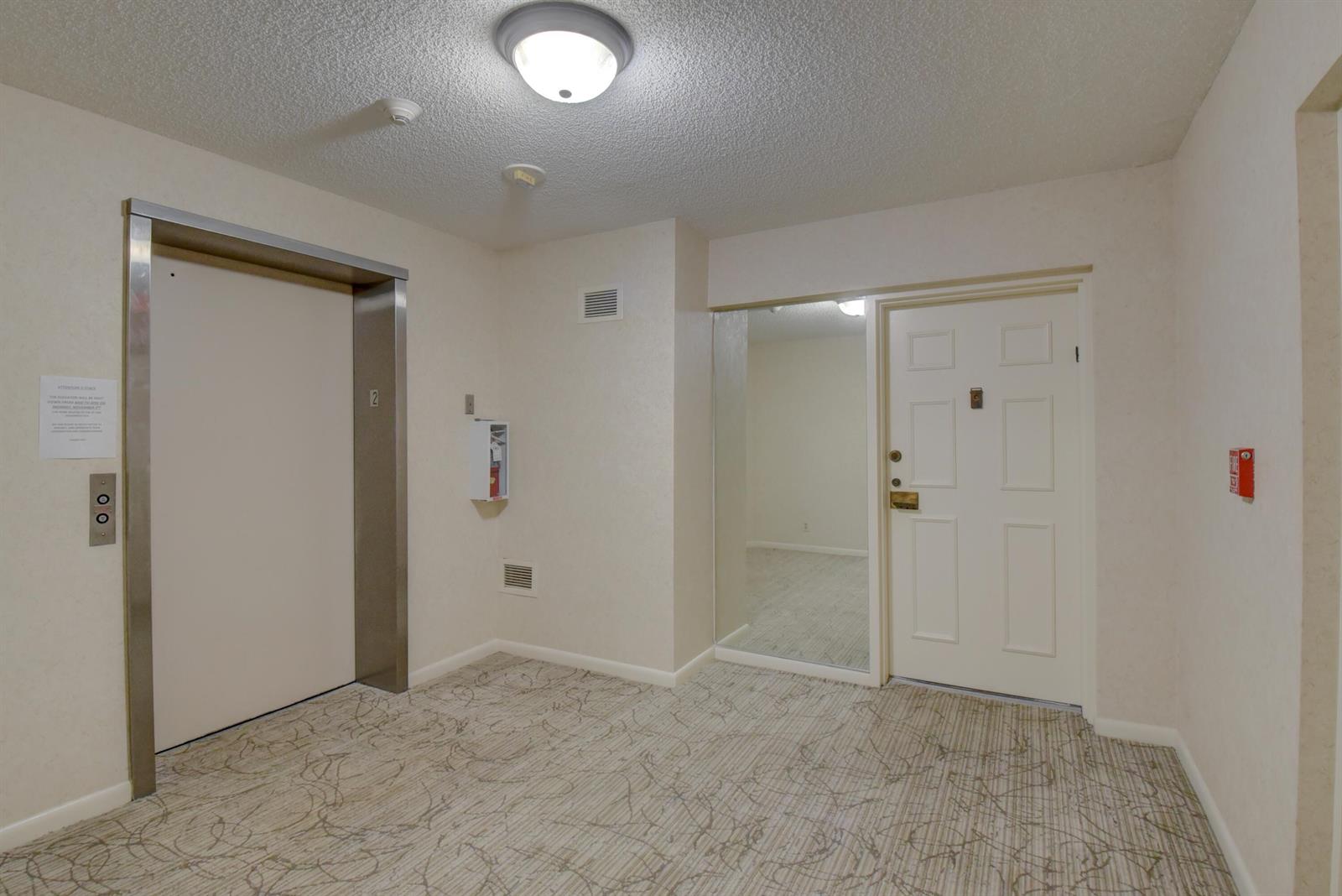 A hallway features a carpeted floor, an elevator, a white door, and a mirrored closet — 7194 Promenade Drive # 202, Boca Raton FL 33433, BOCA RATON, FL