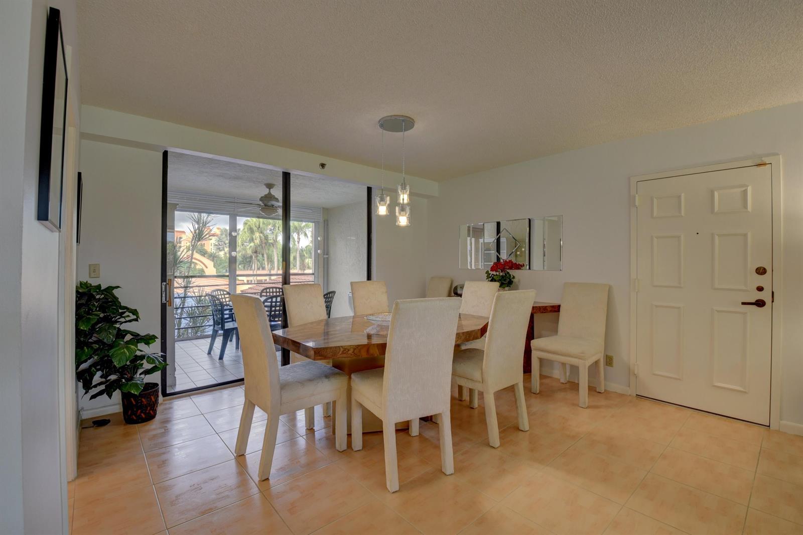 A dining room with a wooden table, six chairs, tile flooring, and a sliding glass door — 7194 Promenade Drive # 202, Boca Raton FL 33433, BOCA RATON, FL
