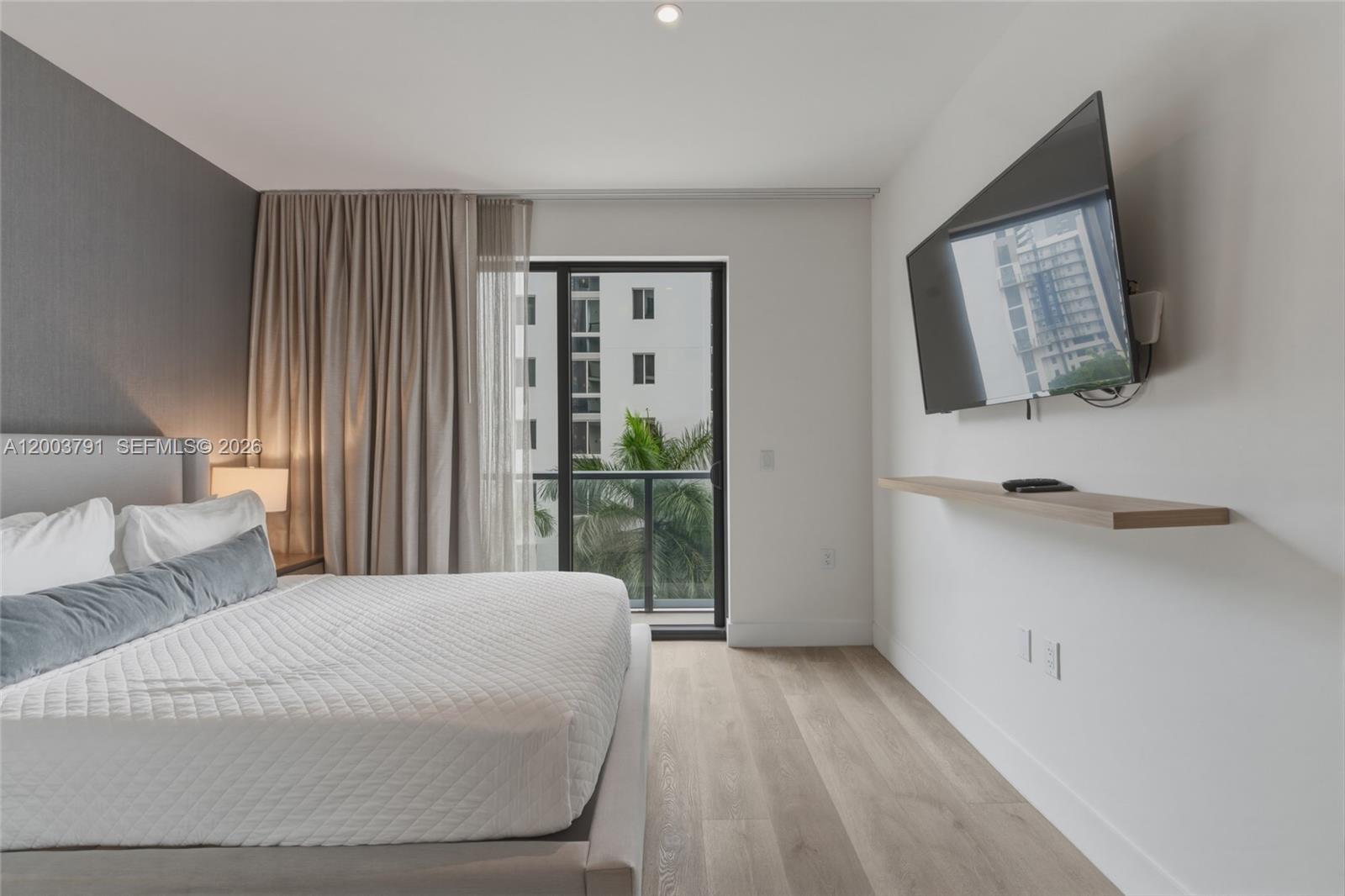 A modern bedroom features a bed, a wall-mounted television, and a balcony with palm trees — 229 SW 9th St # 502, Miami FL 33130, MIAMI, FL