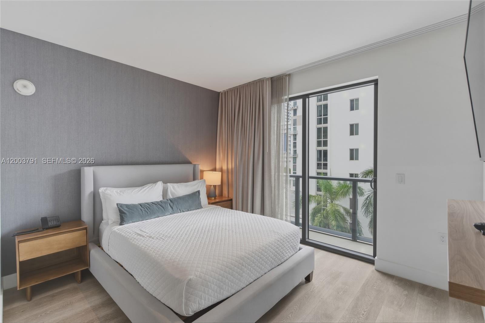A bedroom features a gray upholstered bed, wood nightstands, and a balcony with city views — 229 SW 9th St # 502, Miami FL 33130, MIAMI, FL