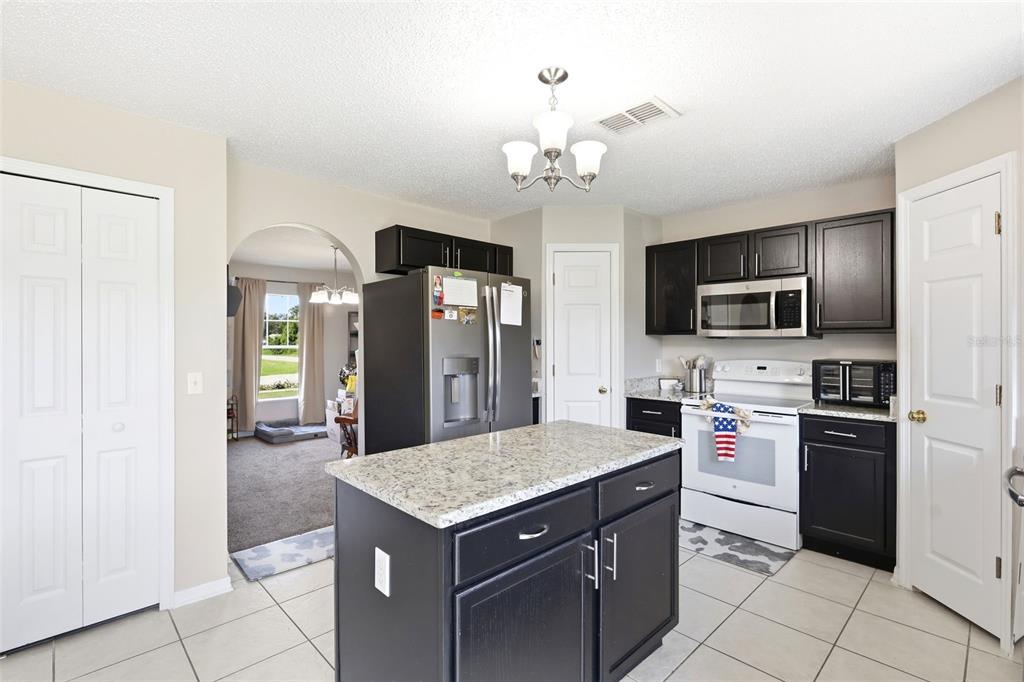 A kitchen features dark cabinets, granite countertops, a center island, and white tile flooring — 2678 BECKWITH STREET, DELTONA, FL