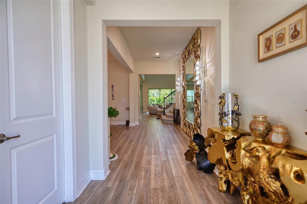 A hallway with wood-look flooring leads to a living area featuring a large gold-framed mirror — 8059 LEAF GROVE CIRCLE, ORLANDO, FL