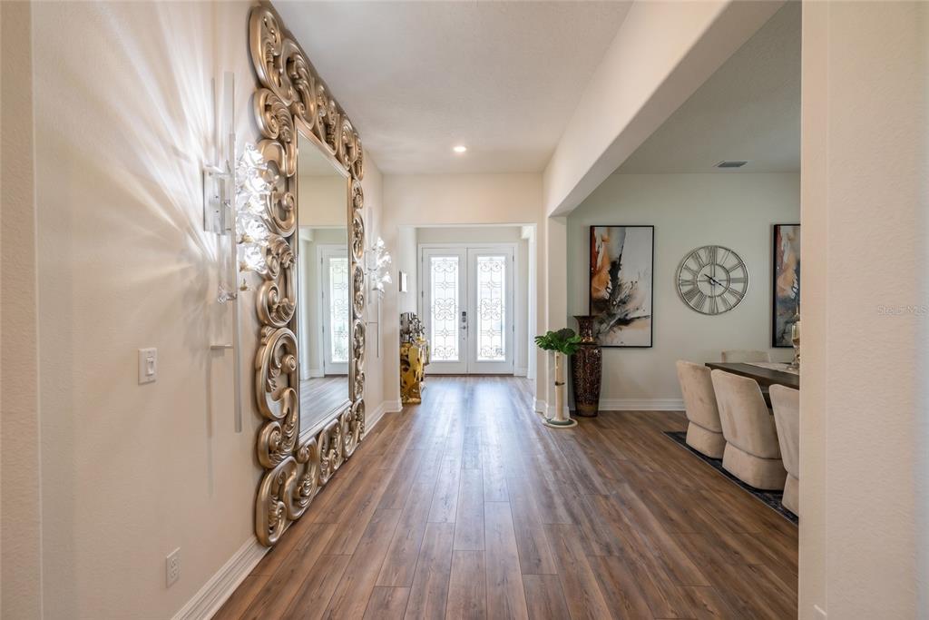A hallway with wood-look flooring leads to a front entryway featuring a large ornate mirror — 8059 LEAF GROVE CIRCLE, ORLANDO, FL