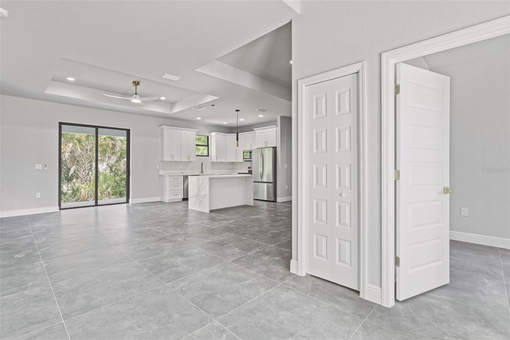 A bright, open-concept kitchen and living area features gray tile flooring and white cabinetry — 2921 BILLBERRY STREET, NORTH PORT, FL