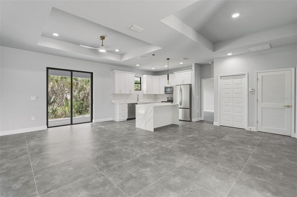 A modern kitchen and living area with gray tile floors, white cabinets, and sliding doors — 2921 BILLBERRY STREET, NORTH PORT, FL
