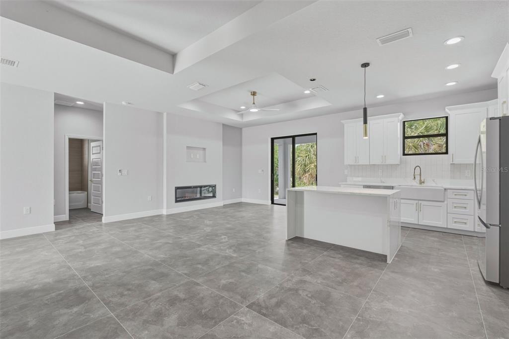 A modern open-concept kitchen and living area featuring white cabinetry, gray tile flooring, and a fireplace — 2921 BILLBERRY STREET, NORTH PORT, FL