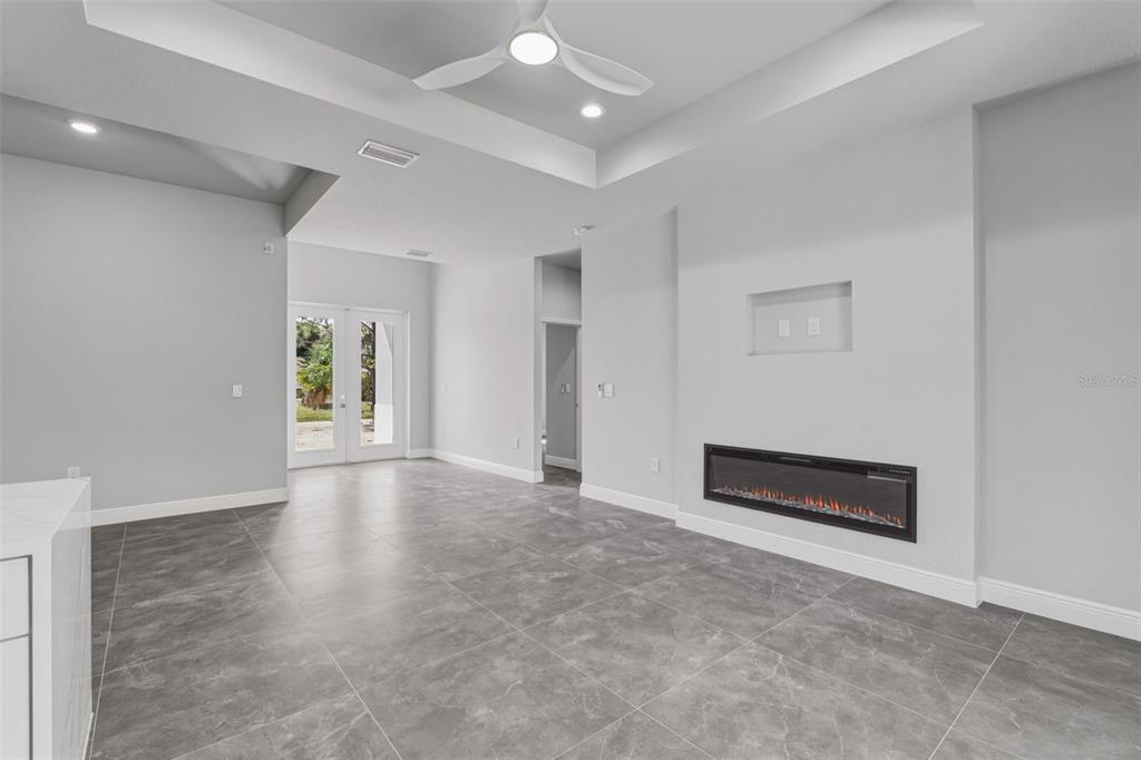 A living room with gray tile flooring, a recessed ceiling, and a wall-mounted electric fireplace — 2921 BILLBERRY STREET, NORTH PORT, FL
