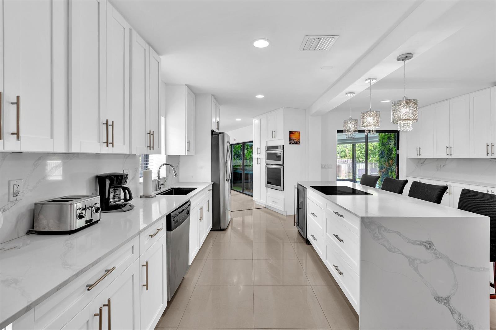 A modern white kitchen features a large marble-topped island, stainless steel appliances, and tile flooring — 5901 W Broward Boulevard, Plantation FL 33317, PLANTATION, FL