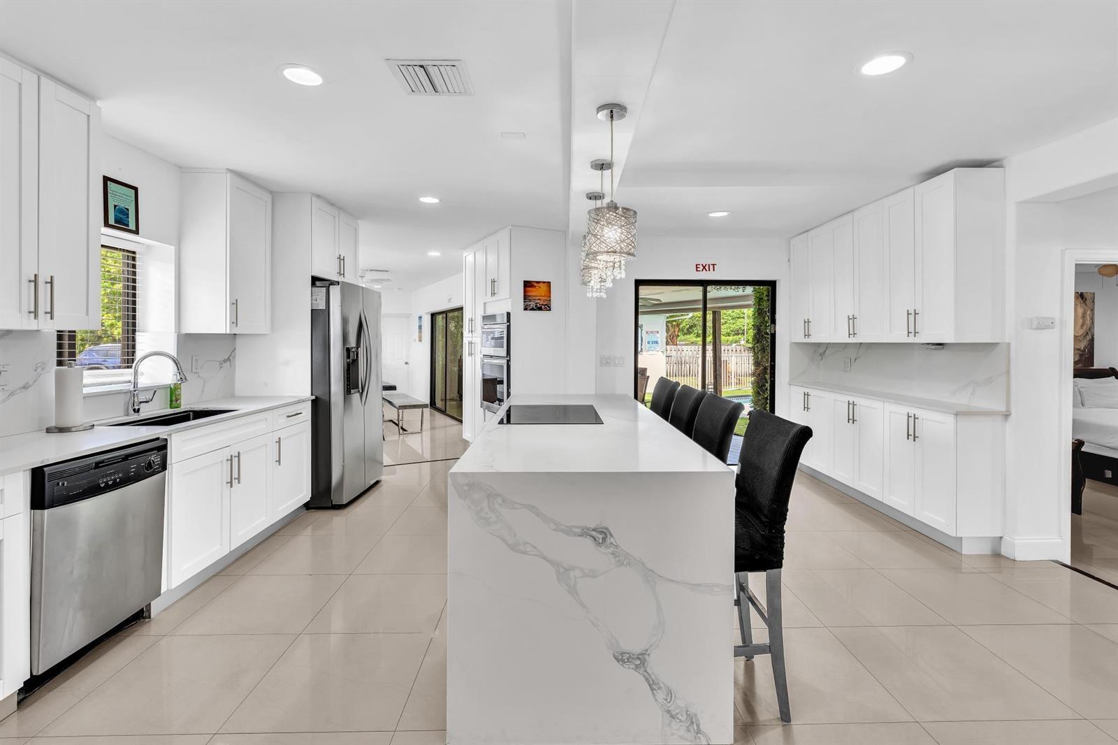 A modern white kitchen features a marble-topped island, stainless steel appliances, and tile flooring — 5901 W Broward Boulevard, Plantation FL 33317, PLANTATION, FL