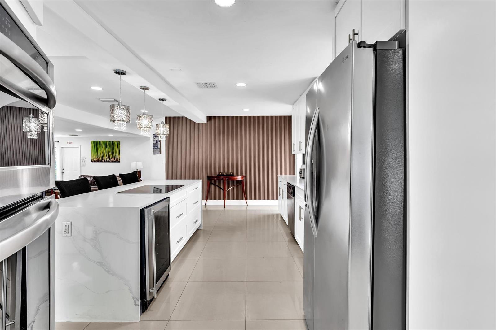 A modern kitchen features white cabinets, a marble-topped island, stainless steel appliances, and tile flooring — 5901 W Broward Boulevard, Plantation FL 33317, PLANTATION, FL