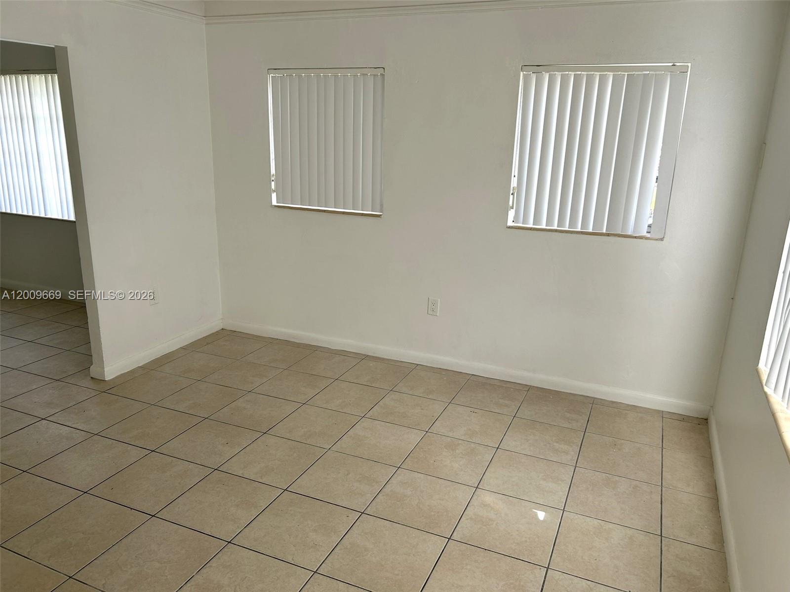 An empty room features white walls, tan tile flooring, and three windows with vertical blinds — 9808 NW 2nd Ave, Miami FL 33150, MIAMI, FL