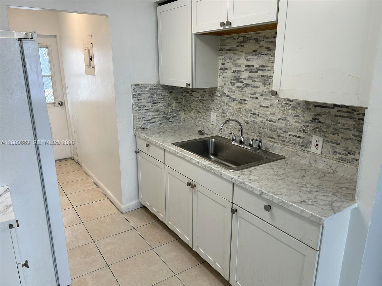 A kitchen features white cabinets, a marble-patterned countertop, and a gray mosaic tile backsplash — 9808 NW 2nd Ave, Miami FL 33150, MIAMI, FL