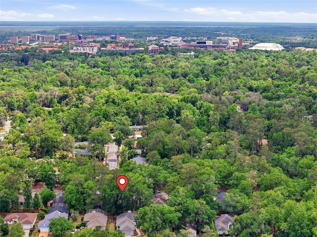 An aerial view shows a residential neighborhood surrounded by dense trees with a city skyline — 1736 NW 16TH PLACE, GAINESVILLE, FL