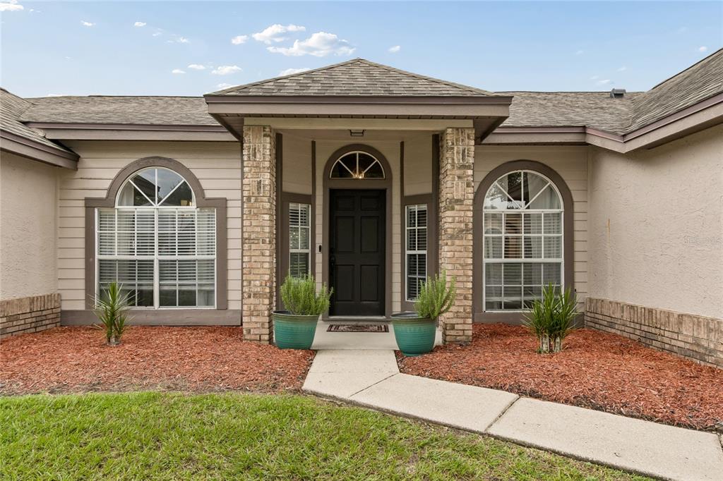 The exterior of a single-story house features a brick-accented entryway, arched windows, and a walkway — 1552 THORNHILL CIRCLE, OVIEDO, FL