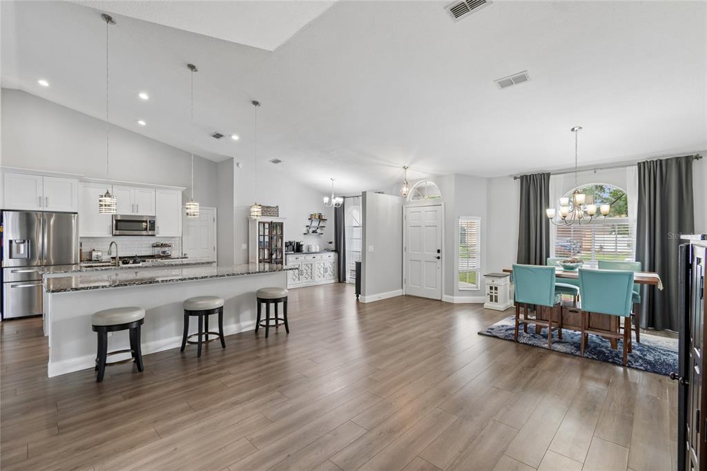 An open-concept kitchen and dining area with white cabinetry, granite countertops, and wood-look flooring — 1552 THORNHILL CIRCLE, OVIEDO, FL
