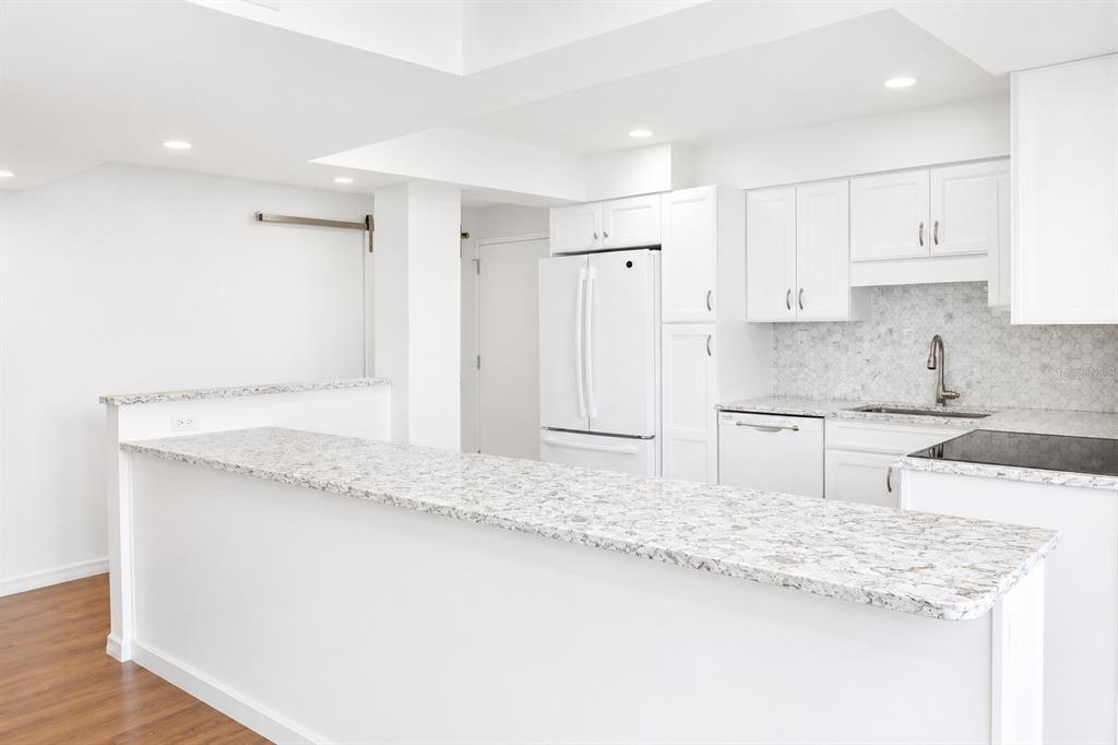 A white kitchen island with marble countertops overlooks a bright living area with ocean views — 707 S GULFSTREAM AVENUE UNIT 307, SARASOTA, FL
