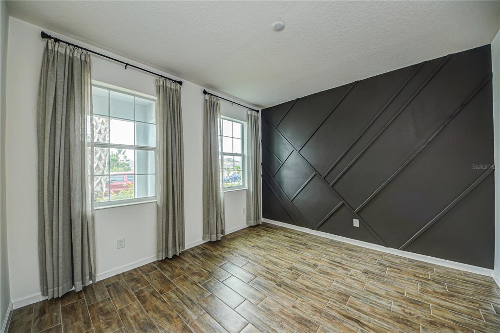 A room with wood-look tile flooring, two windows with curtains, and a dark geometric accent wall — 603 FORTUNA DRIVE, DAVENPORT, FL