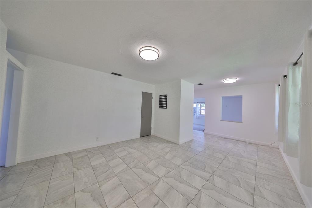 A bright, empty room features white walls, light-colored tiled floors, and two flush-mount ceiling lights — 3908 W WALLACE AVENUE, TAMPA, FL