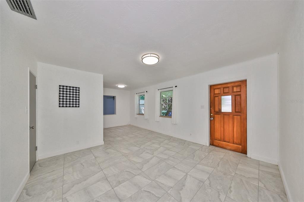 A bright living room features white walls, light-colored tile flooring, and a wooden front door — 3908 W WALLACE AVENUE, TAMPA, FL