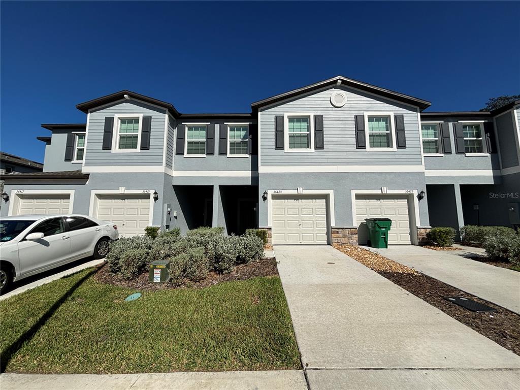 A two-story townhouse exterior features light blue siding, white garage doors, and a concrete driveway — 36425 CAMPFIRE TERRACE, ZEPHYRHILLS, FL