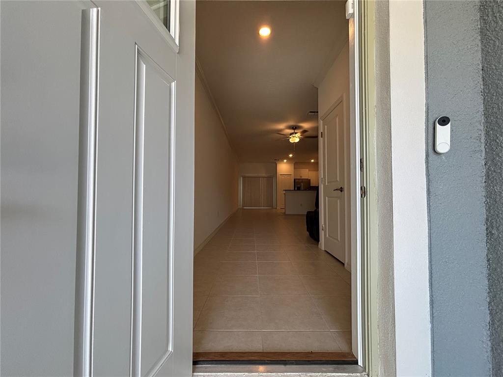 A view through an open front door reveals a tiled hallway leading to a kitchen — 36425 CAMPFIRE TERRACE, ZEPHYRHILLS, FL