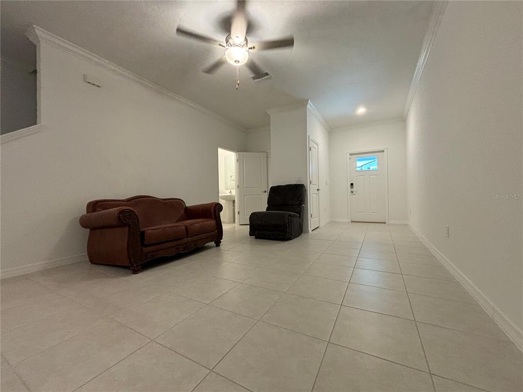 An unfurnished living room features white walls, tile flooring, a ceiling fan, and two chairs — 36425 CAMPFIRE TERRACE, ZEPHYRHILLS, FL