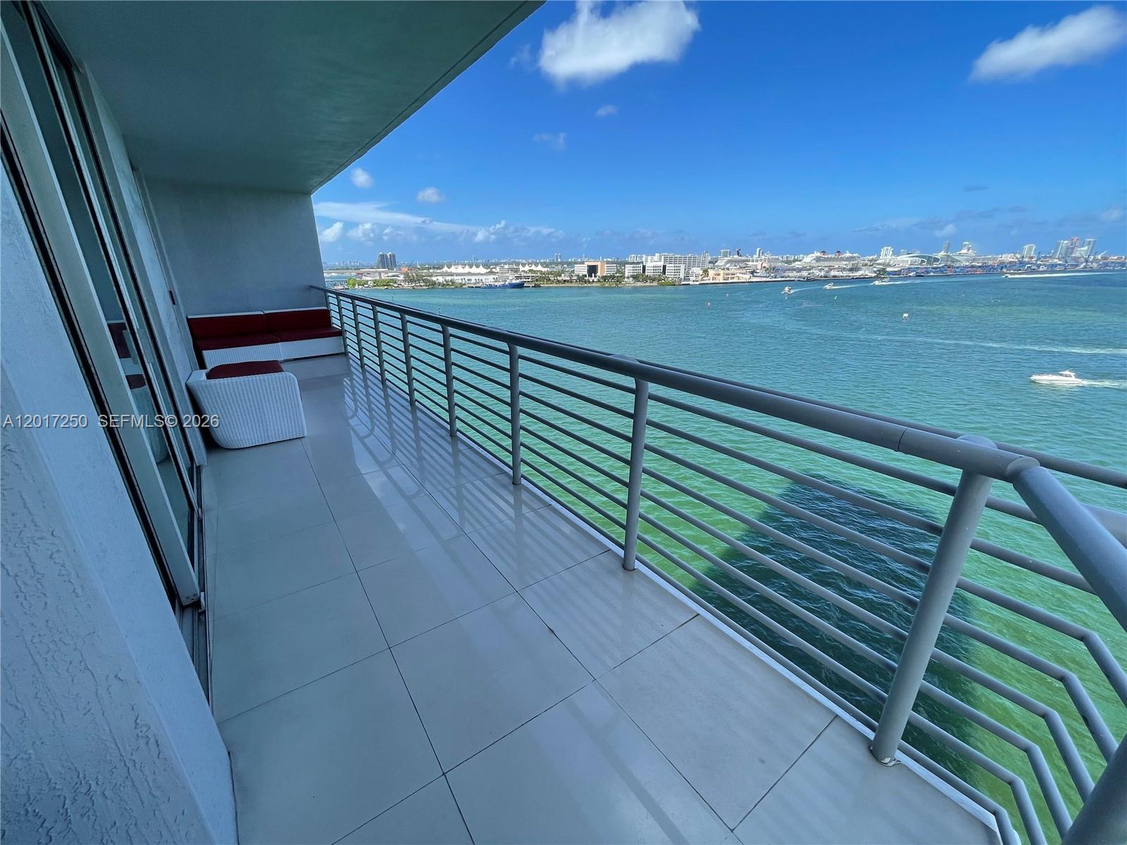 A balcony with tiled flooring, metal railings, and outdoor seating overlooks a bay and city — 335 S Biscayne Blvd # 1209, Miami FL 33131, MIAMI, FL