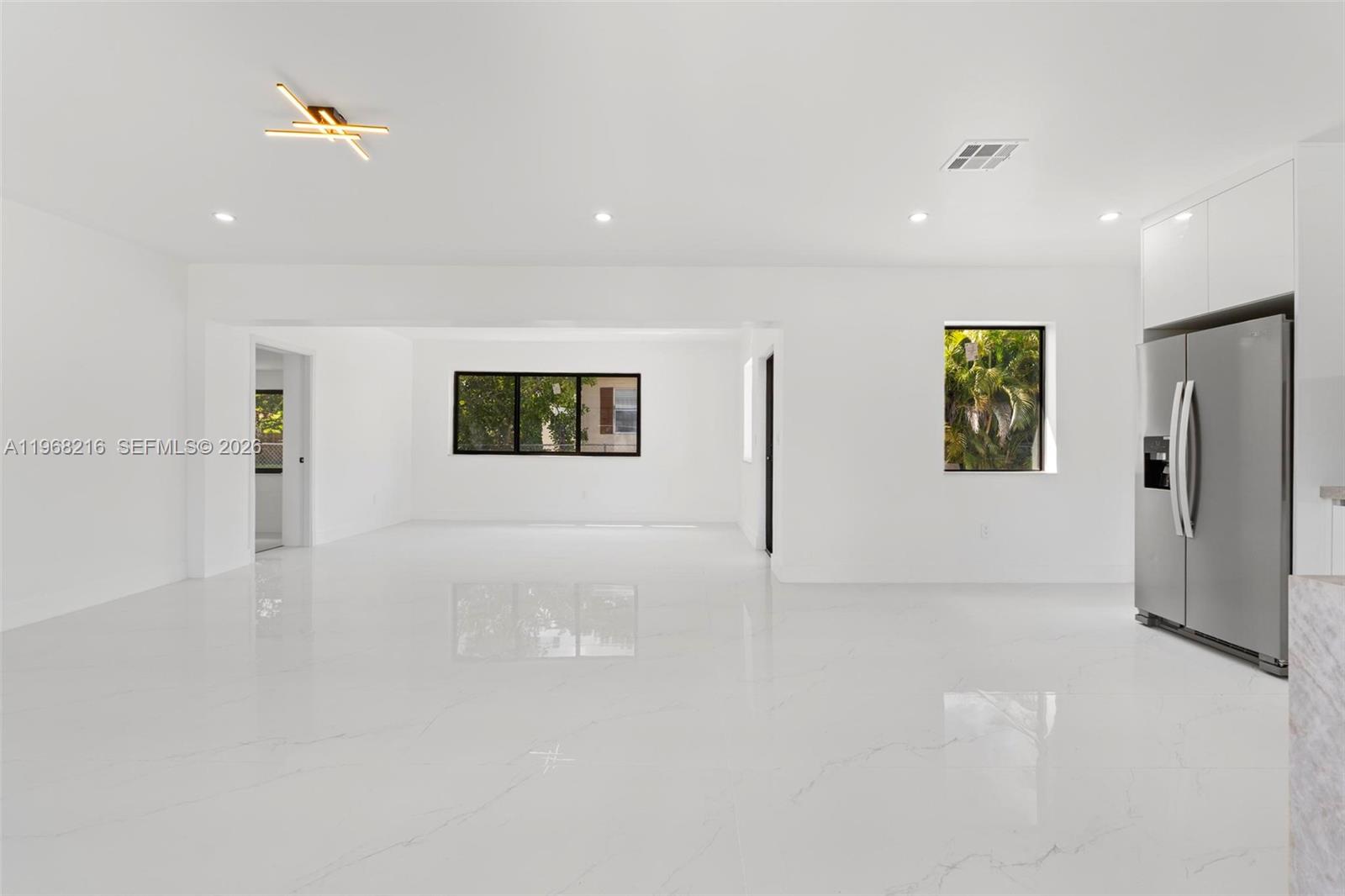 A bright, open-concept kitchen and living area features white walls, glossy marble-look tile floors, and a stainless steel refrigerator — 14950 NE 2nd Ave, Miami FL 33161, MIAMI, FL