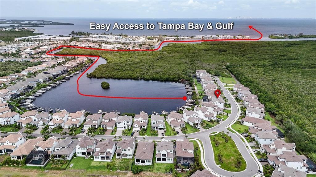 An aerial view shows a residential neighborhood with a canal leading to open water — 1108 SEAGRAPE DRIVE, RUSKIN, FL