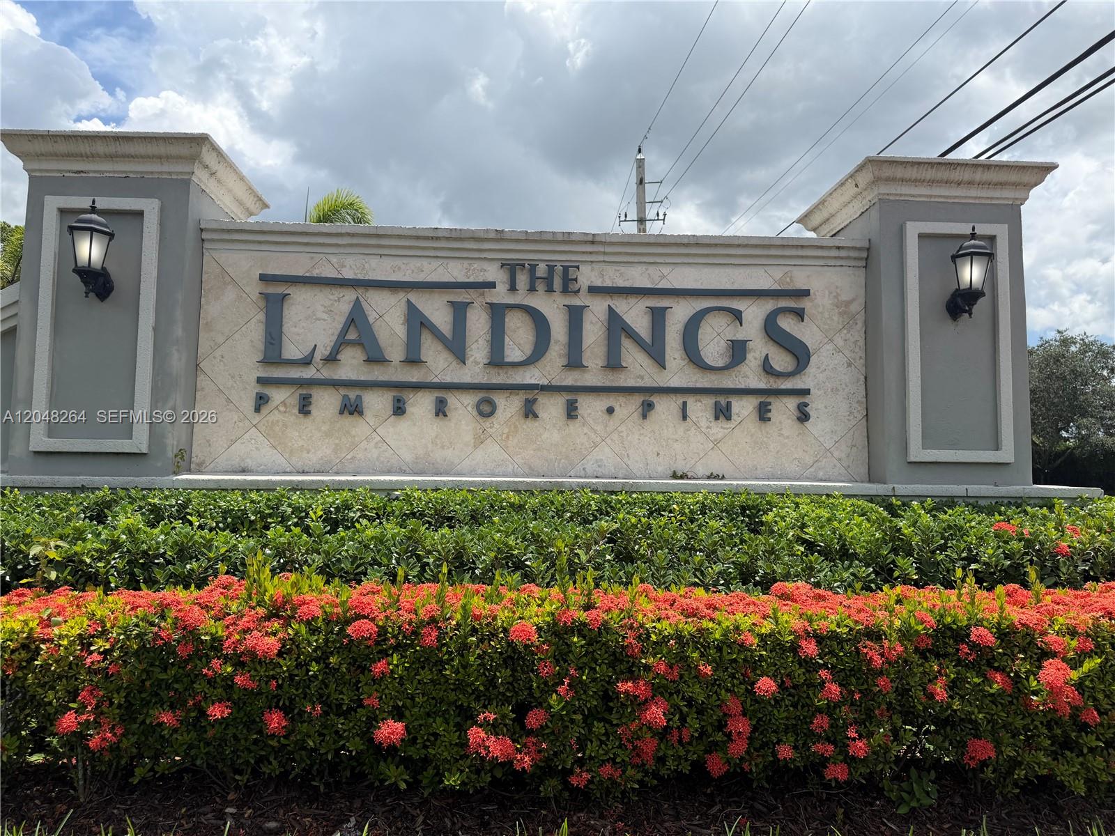 A stone monument sign for The Landings in Pembroke Pines sits behind a flowering hedge — PEMBROKE PINES, FL