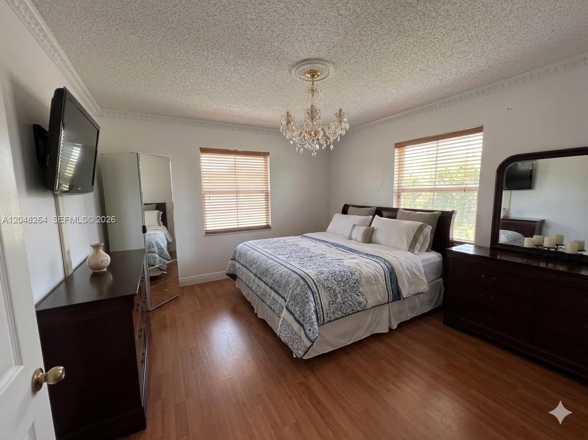 A bedroom features a bed, two dressers, a chandelier, and wood-look flooring — PEMBROKE PINES, FL