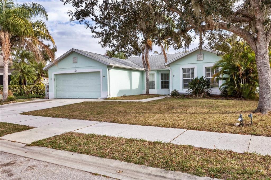 A light green, single-story suburban house with a two-car garage and a large oak tree — 11619 SUMMIT ROCK COURT, PARRISH, FL