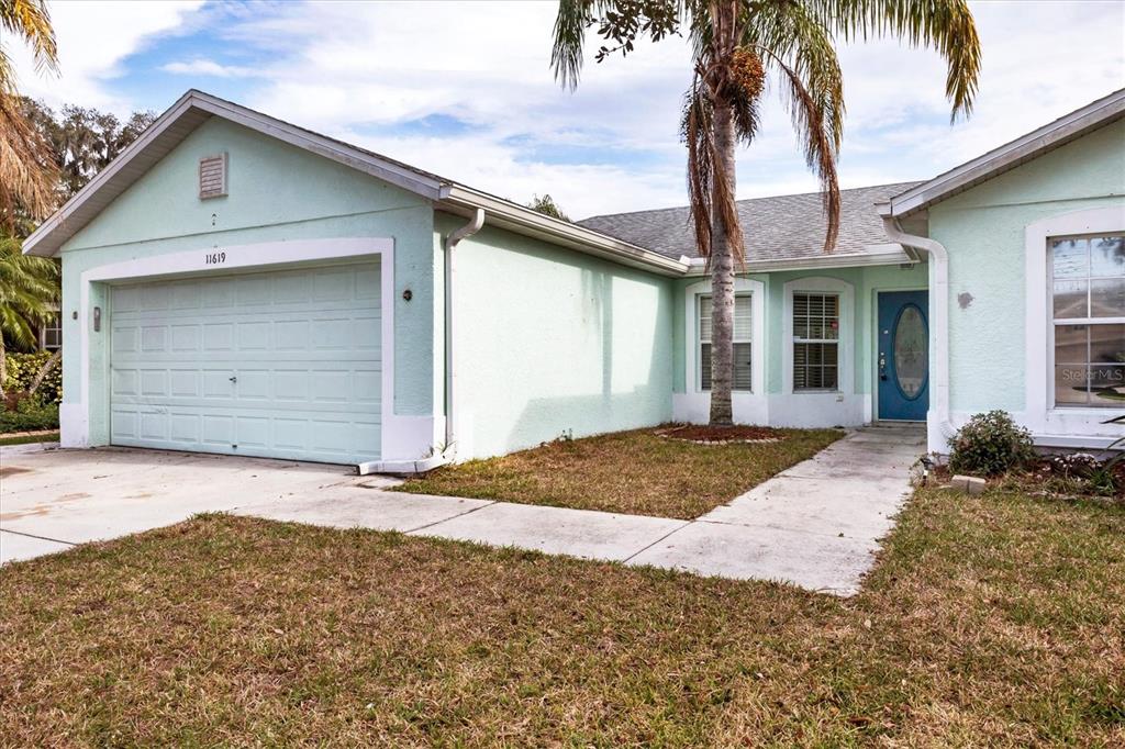 A light green single-story house with a two-car garage and a blue front door — 11619 SUMMIT ROCK COURT, PARRISH, FL