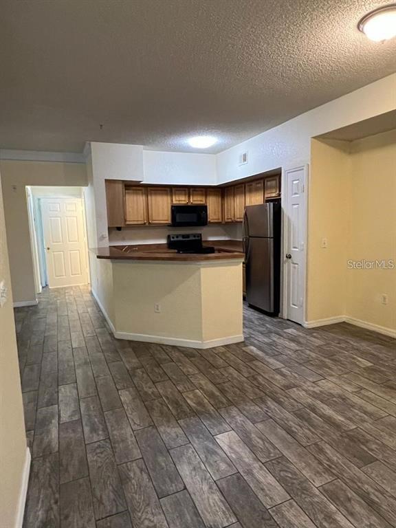 A kitchen with wood cabinets, stainless steel appliances, and a breakfast bar over wood-look flooring — 13025 MULBERRY PARK DRIVE UNIT 311, ORLANDO, FL