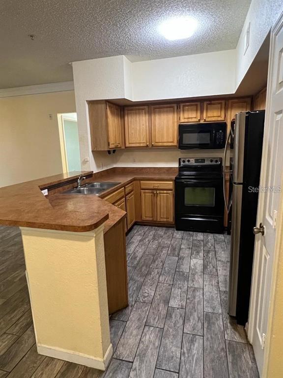 A kitchen features wood cabinets, laminate countertops, black appliances, and gray wood-look tile flooring — 13025 MULBERRY PARK DRIVE UNIT 311, ORLANDO, FL
