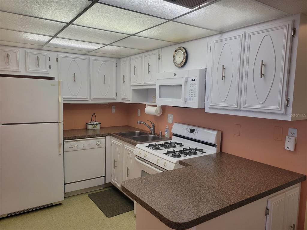A kitchen with white cabinets, a white refrigerator, a gas stove, and peach-colored walls — 9950 62ND TERRACE N UNIT 417, ST PETERSBURG, FL