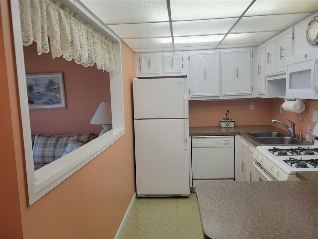 A kitchen with white cabinets, white appliances, and a pass-through window looking into a room — 9950 62ND TERRACE N UNIT 417, ST PETERSBURG, FL