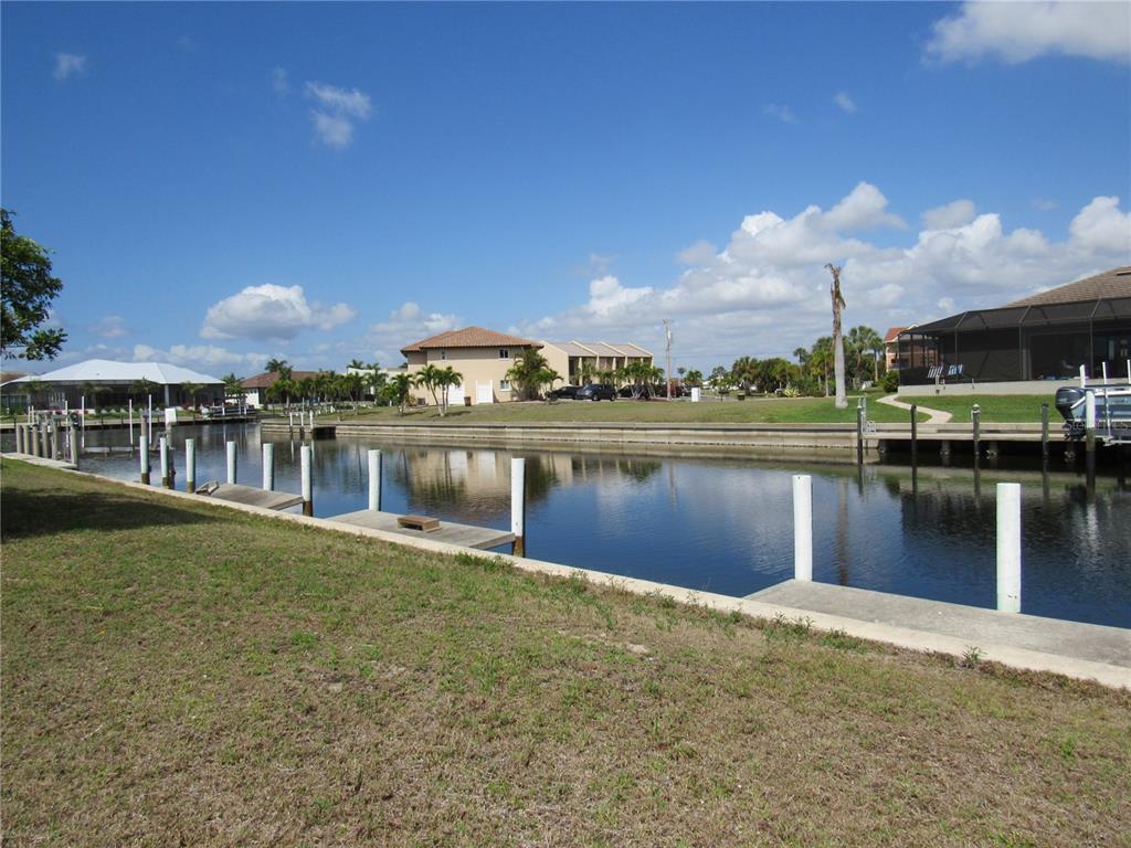 A canal view featuring a grassy lawn, wooden boat docks, and nearby residential houses — 2818 & 2824 MAGDALINA DRIVE, PUNTA GORDA, FL