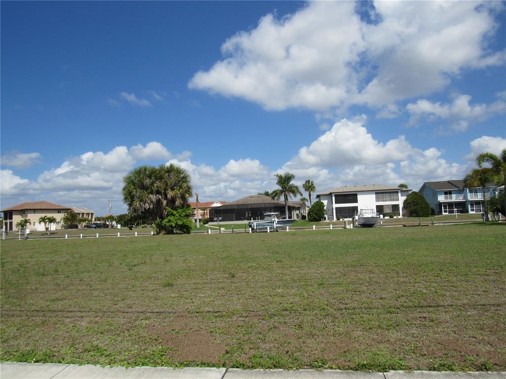 A vacant grassy lot sits in front of several houses and a canal — 2818 & 2824 MAGDALINA DRIVE, PUNTA GORDA, FL
