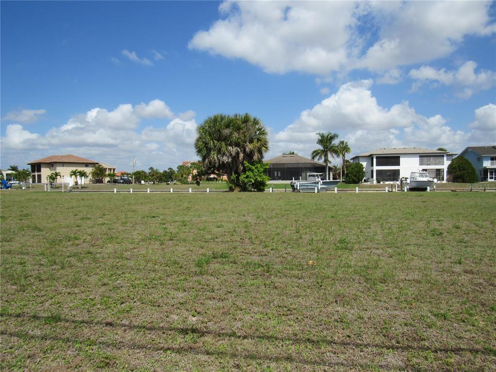 A grassy vacant lot faces a canal with several houses and boats in the background — 2818 & 2824 MAGDALINA DRIVE, PUNTA GORDA, FL
