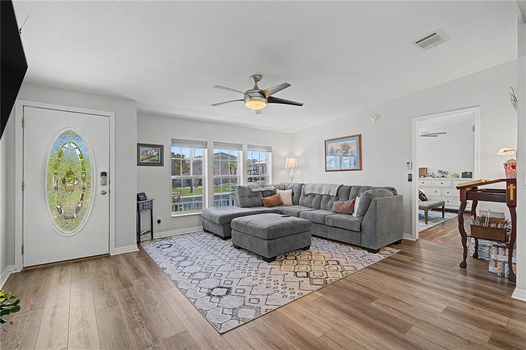 A living room features light wood flooring, a grey sectional sofa, and a patterned rug — 37602 LILLY BEA AVENUE, ZEPHYRHILLS, FL