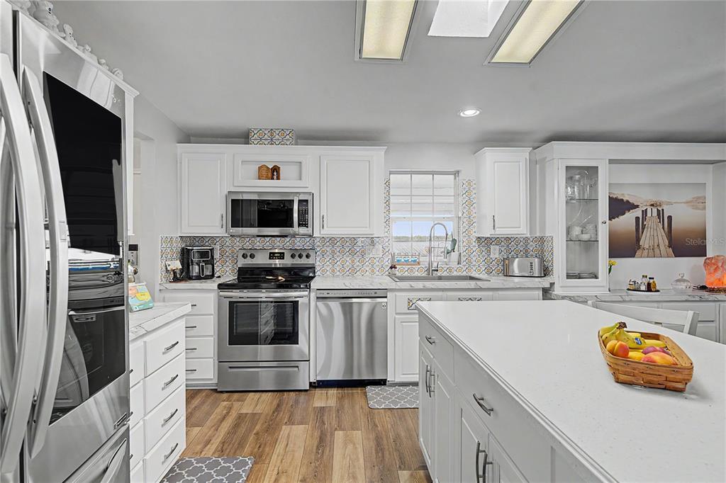 A white kitchen features stainless steel appliances, a center island, and patterned tile backsplashes — 37602 LILLY BEA AVENUE, ZEPHYRHILLS, FL