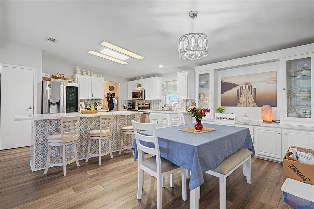 A kitchen and dining area features white cabinetry, a patterned island, and wood-look flooring — 37602 LILLY BEA AVENUE, ZEPHYRHILLS, FL