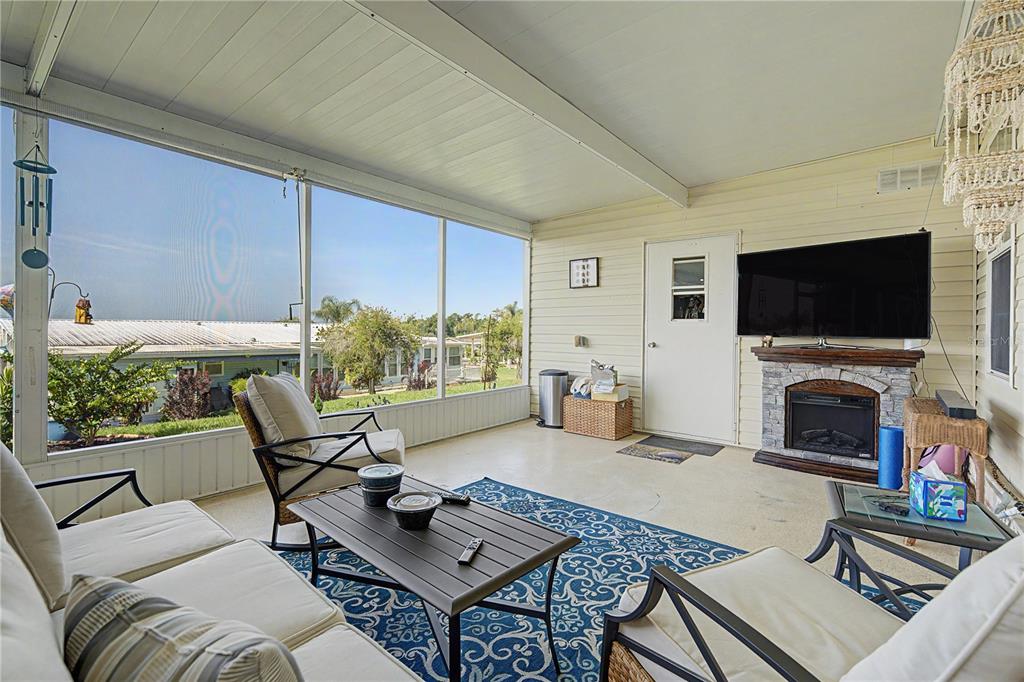 A screened-in porch features a fireplace, a television, outdoor furniture, and a blue patterned rug — 37602 LILLY BEA AVENUE, ZEPHYRHILLS, FL