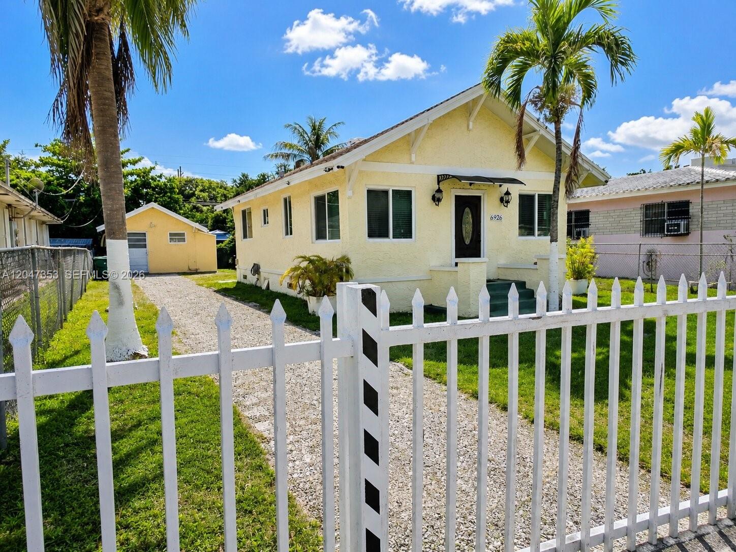 A yellow single-story house with a white picket fence and a gravel driveway — 6926 NW 4th Ave, Miami FL 33150, MIAMI, FL