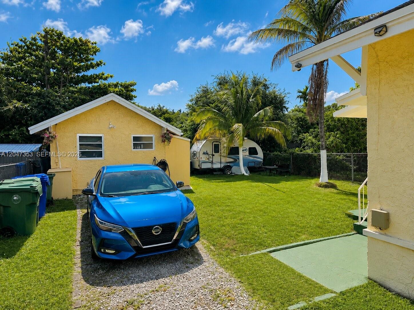 A blue car is parked on a gravel driveway next to a yellow house and yard — 6926 NW 4th Ave, Miami FL 33150, MIAMI, FL