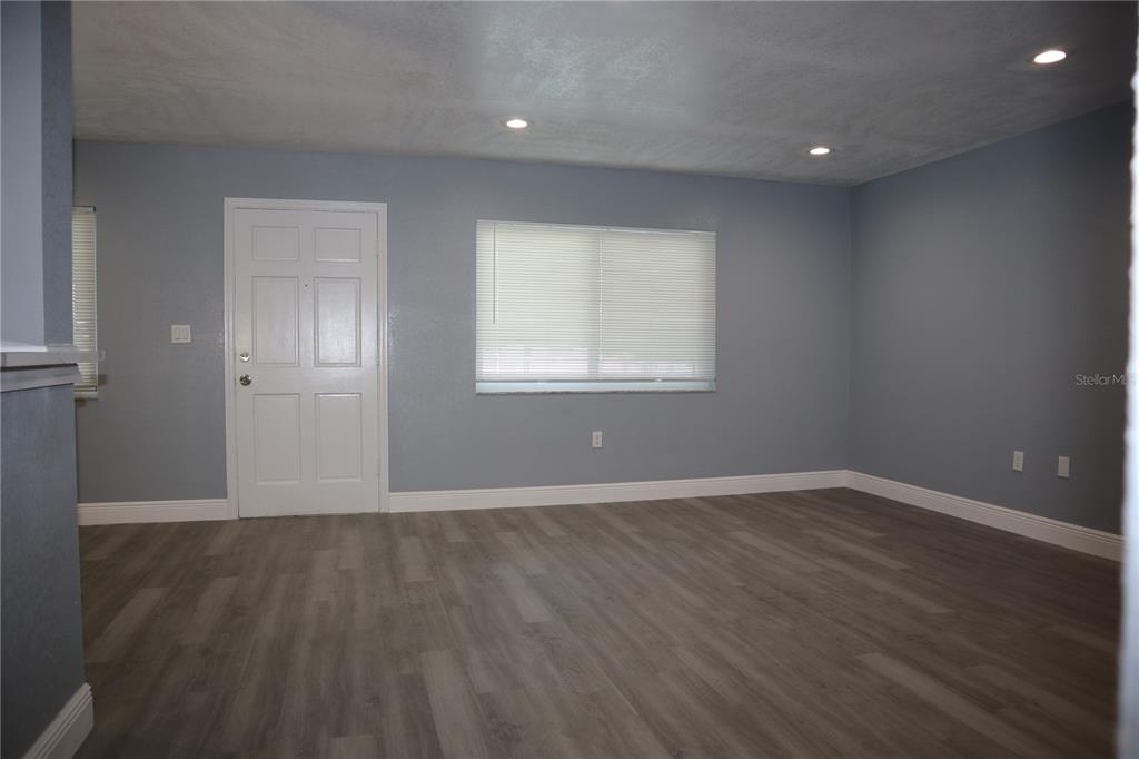 An empty room features gray walls, wood-look flooring, a white door, and a window with blinds — 350 79TH AVENUE N UNIT 236, ST PETERSBURG, FL