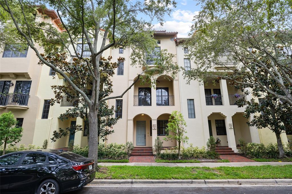 A row of three-story townhomes with arched entryways, balconies, and brick walkways under mature trees — 6039 PRINTERY STREET UNIT 106, TAMPA, FL